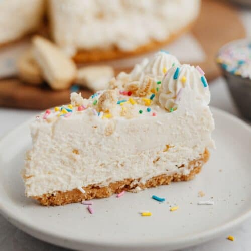 A slice of no bake cheesecake covered in rainbow sprinkles on a small beige plate