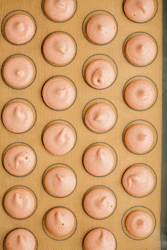Unbaked macaron shells piped out on a macaron silicone mat