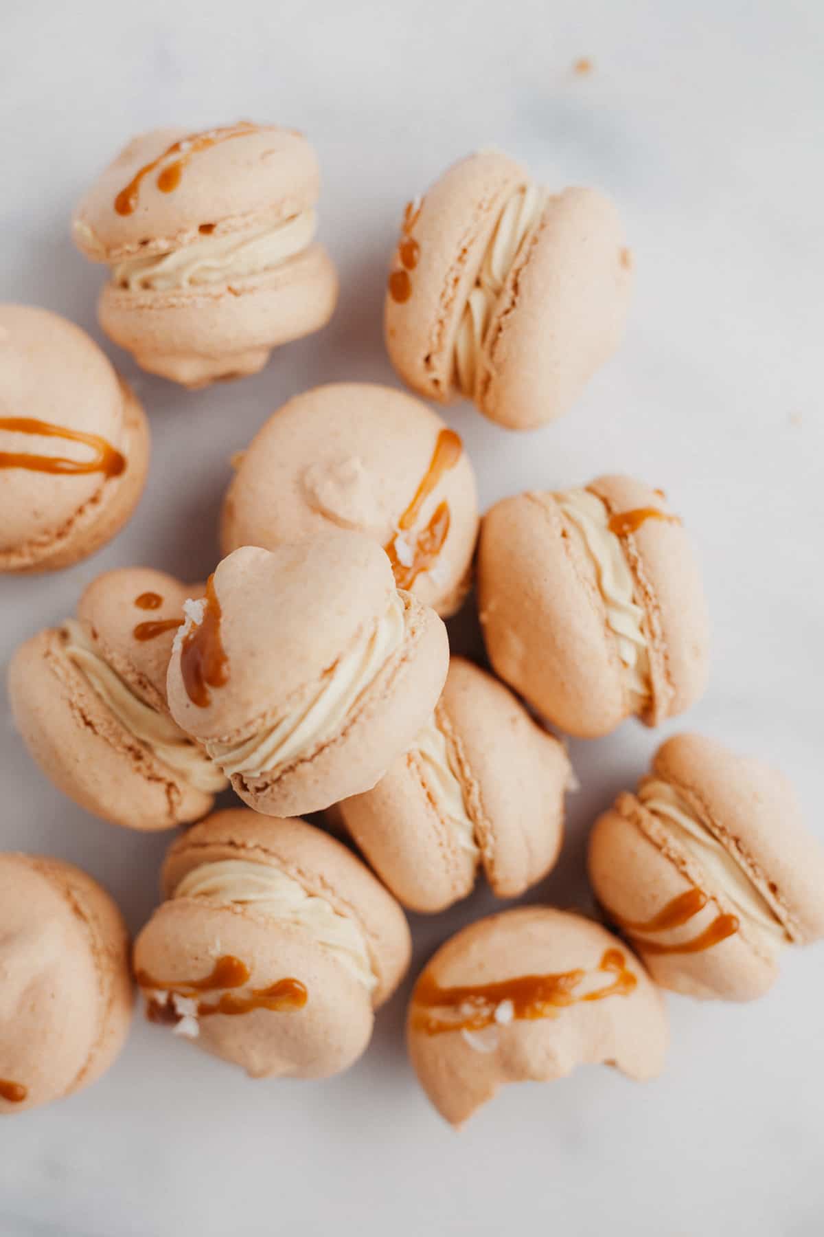 about 10 salted caramel macarons on their side on a marble counter
