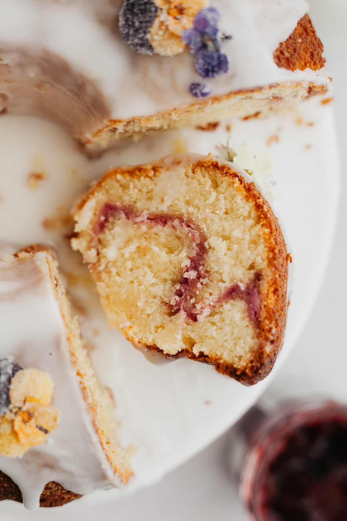 A close up of a slice of bundt cake covered in a white glaze with a raspberry swirl.
