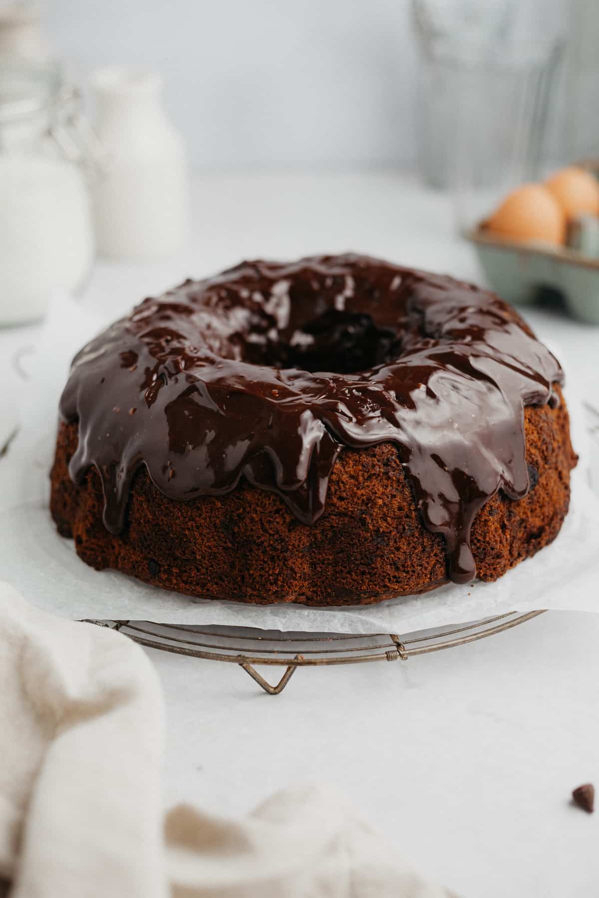 A bundt cake on parchment paper, the cake is covered in a dark chocolate ganache