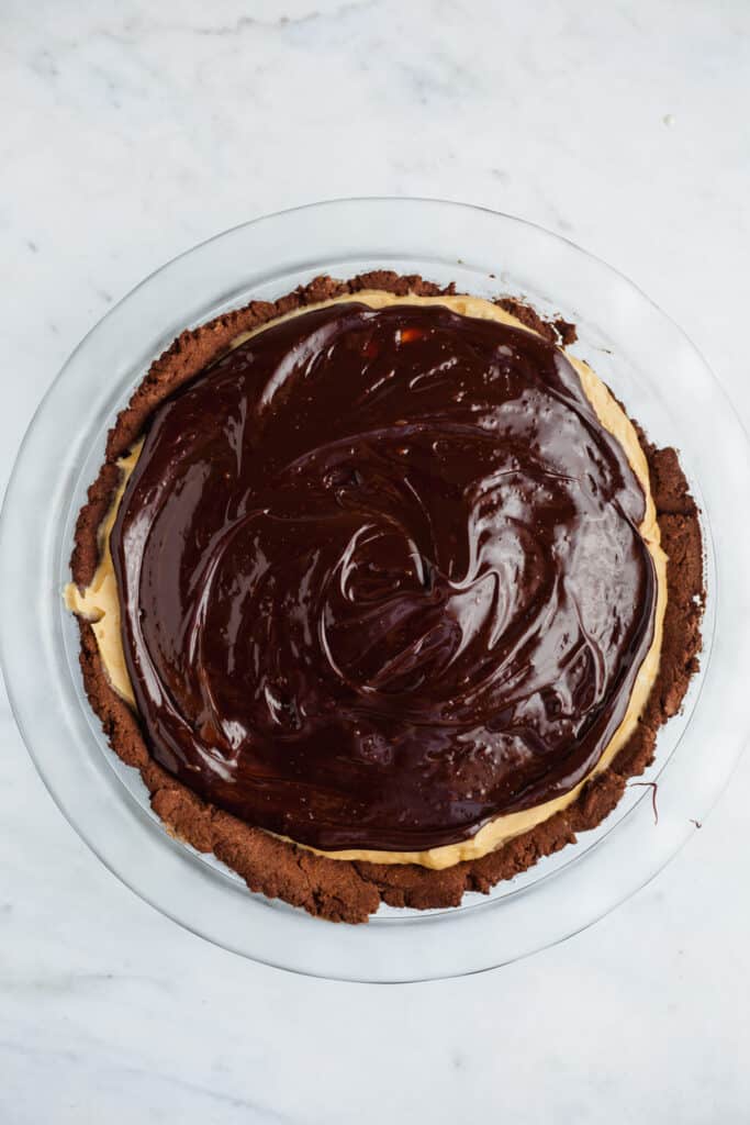 A no bake peanut butter pie in a glass pie plate, covered in chocolate ganache