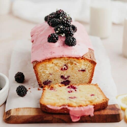 A blackberry lemon loaf sliced, it has a pink glaze and is topped with blackberries.
