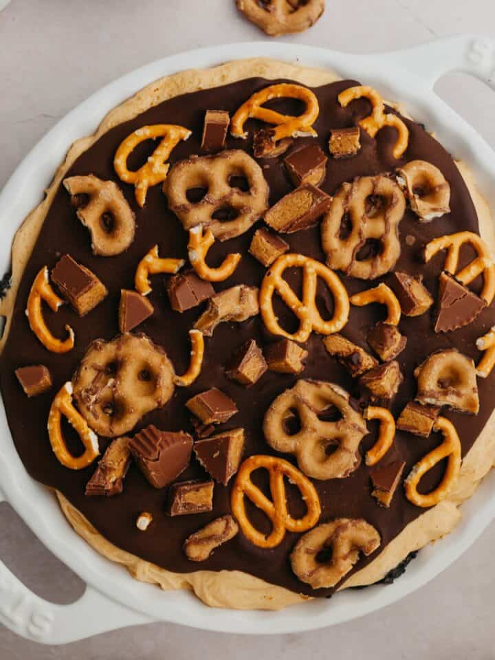 An overhead shot of a pie dish with a peanut butter pie covered in ganache and pretzels.