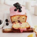A blackberry lemon loaf sliced, it has a pink glaze and is topped with blackberries.