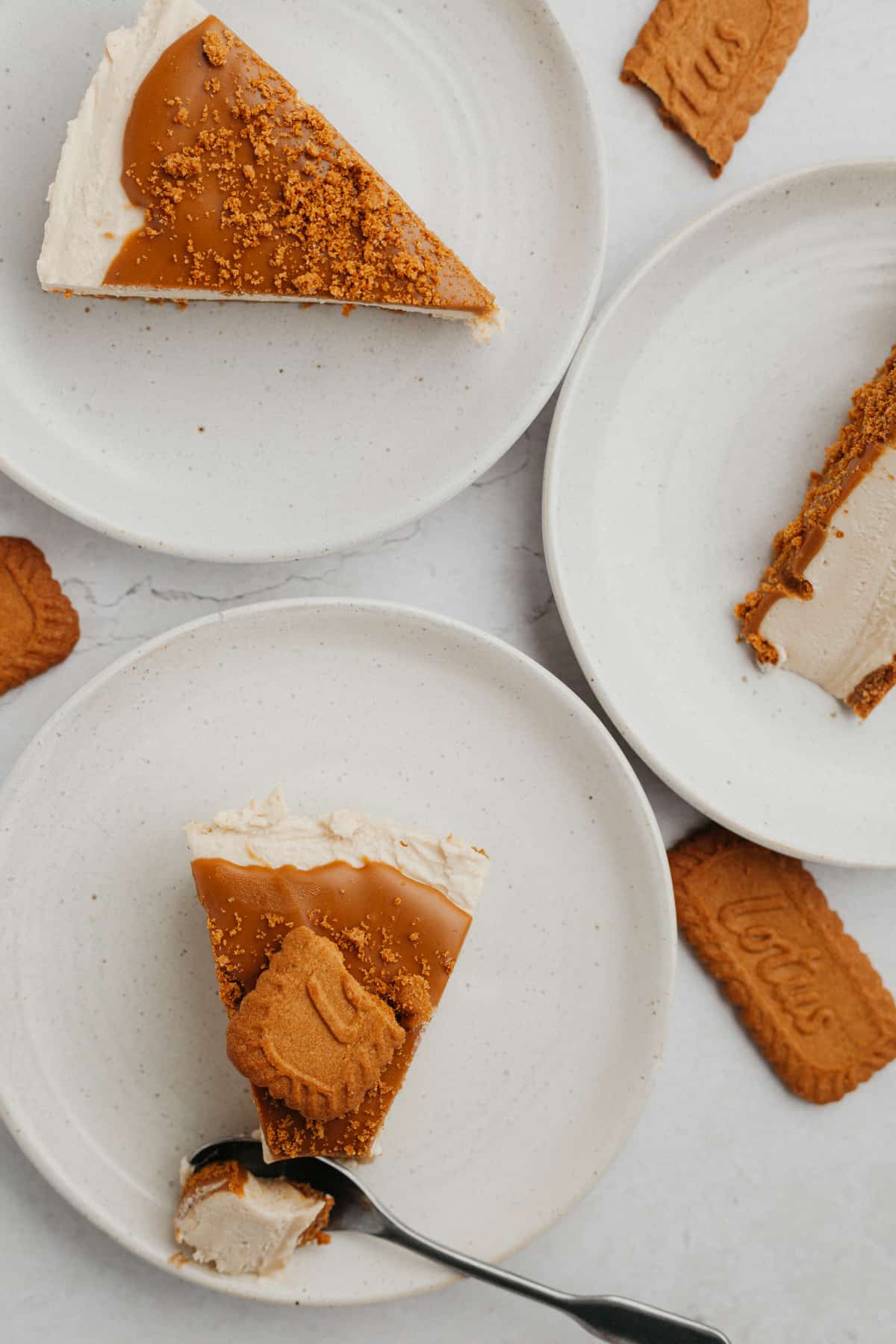 Several small white plates, each one has a slice of Biscoff no bake cheesecake on it.