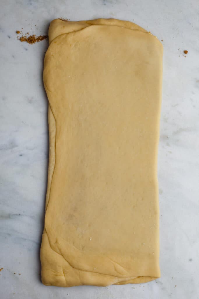 A long rectangular piece of dough on a marble counter