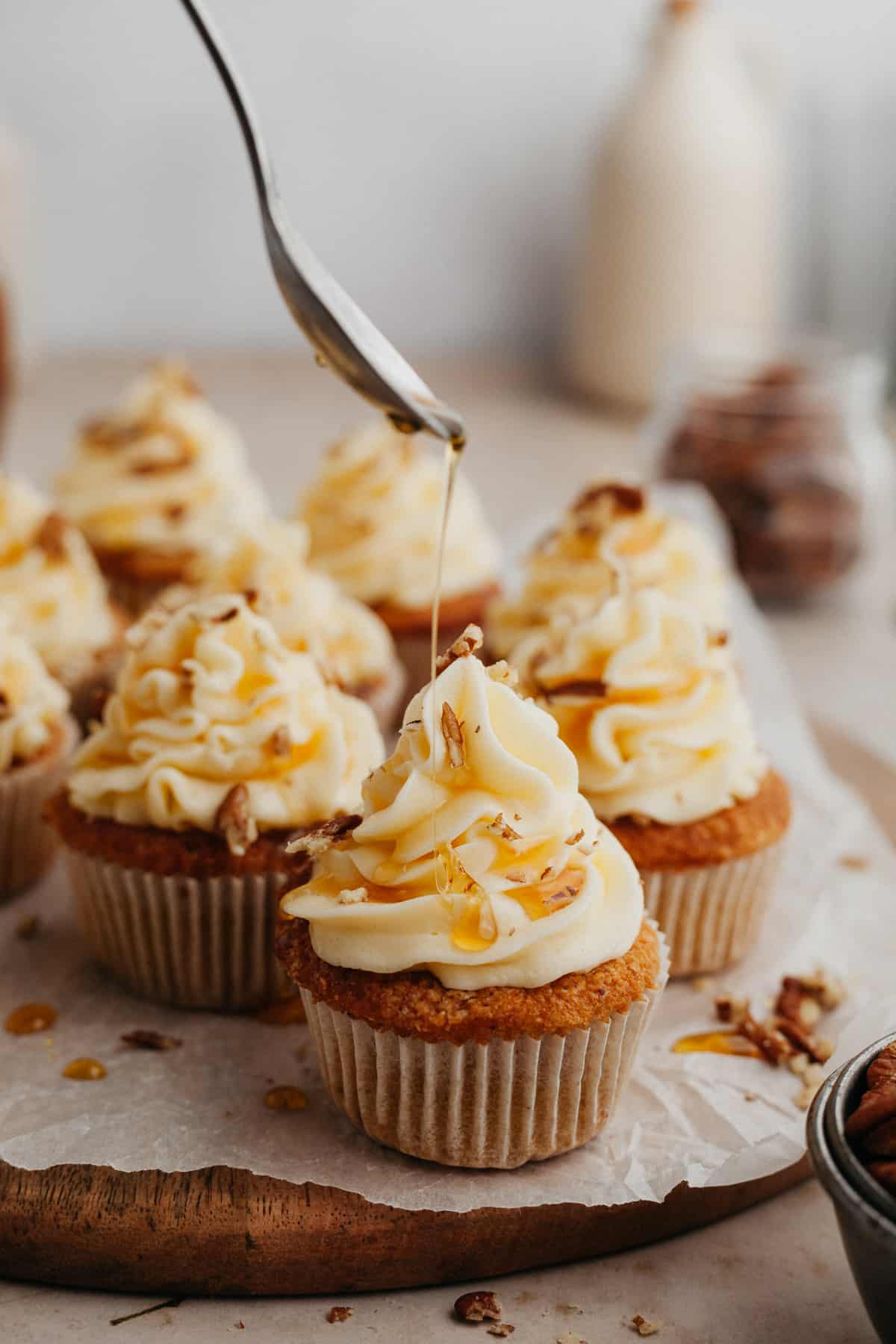 cupcakes with white frosting, the cupcake at the front is being drizzled with maple syrup