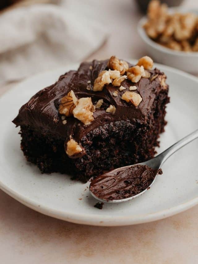 A slice of chocolate walnut cake covered in chocolate frosting and chopped walnuts on a small plate.