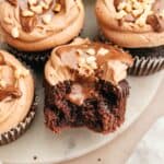 A chocolate cupcake with a bite taken out of it showing it's filled with chocolate.