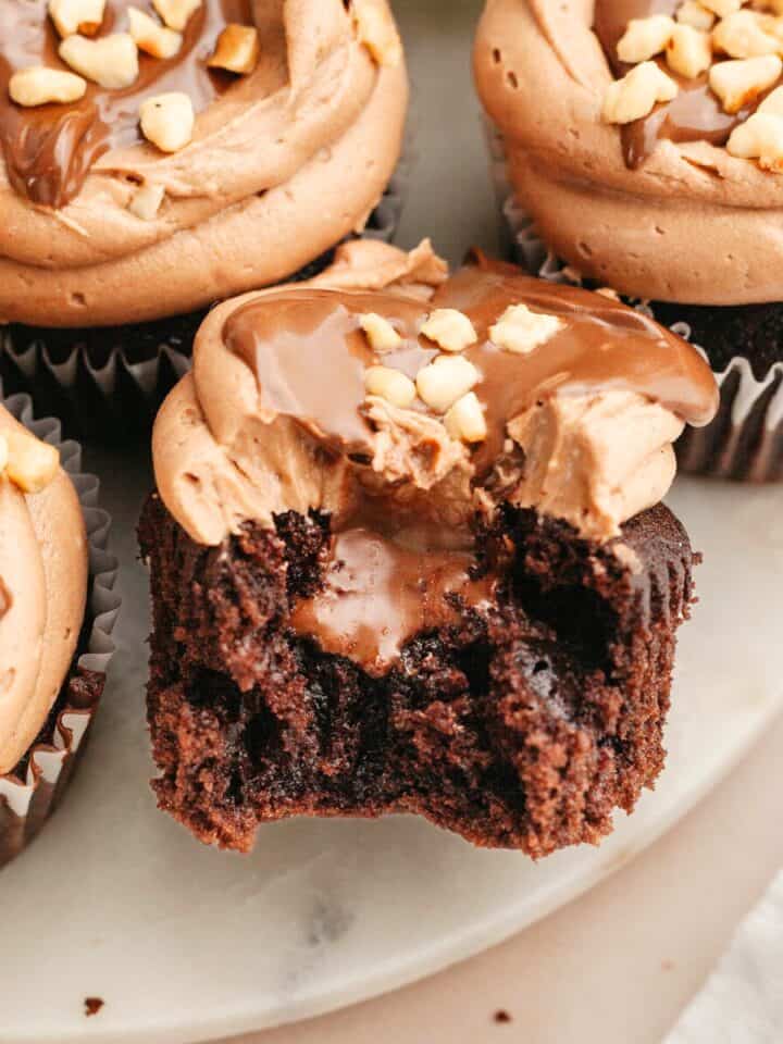 A chocolate cupcake with a bite taken out of it showing it's filled with chocolate.