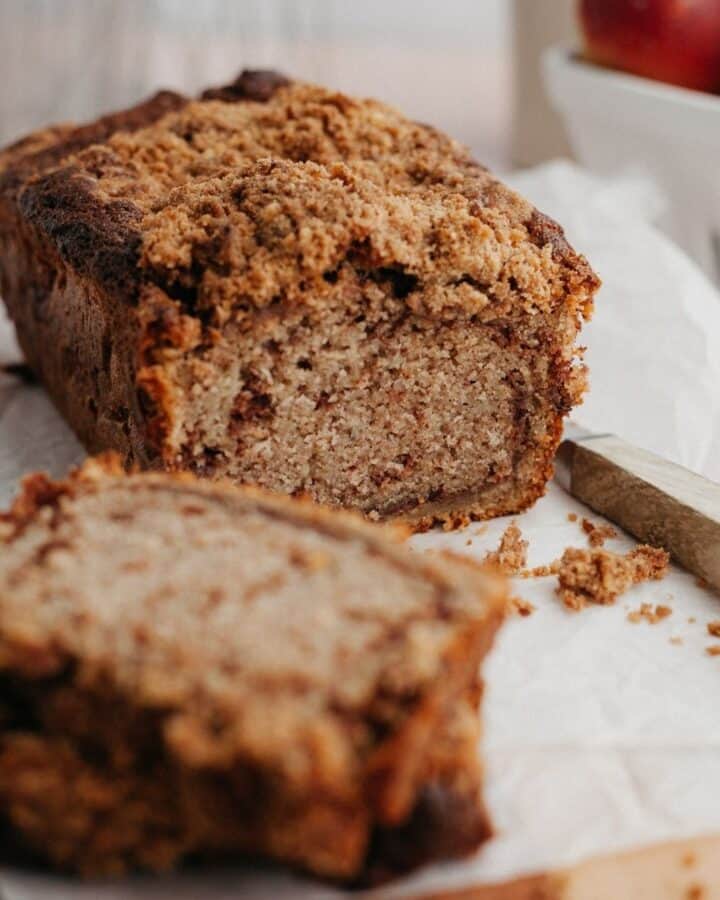 A snickerdoodle apple bread loaf on parchment paper, two slices have been cut off.