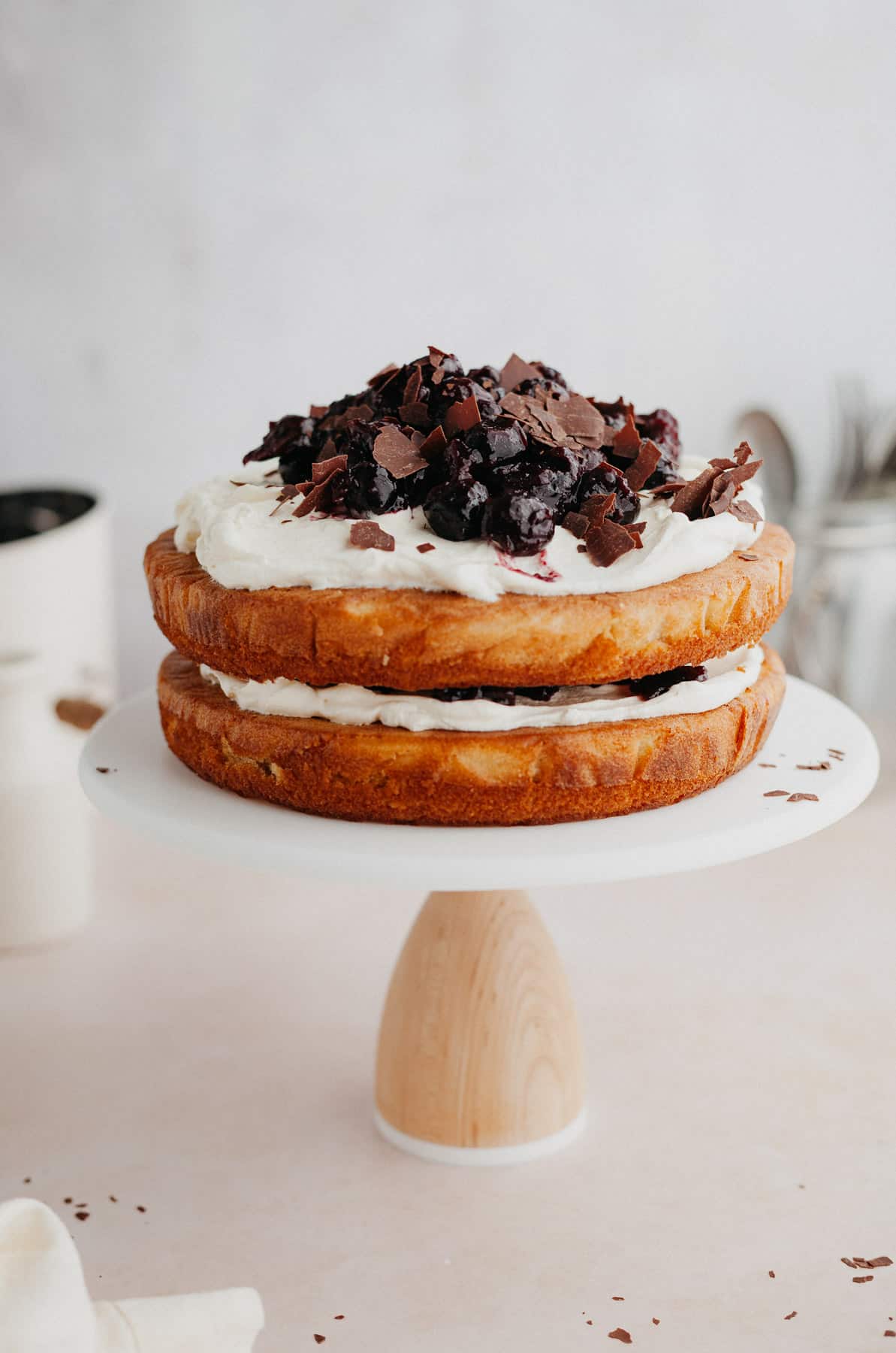 a vanilla black forest cake on a white cake stand.
