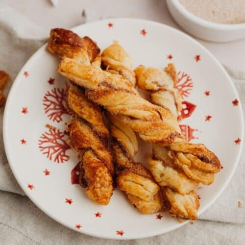 A small red and white plate with cinnamon sugar twists on it.