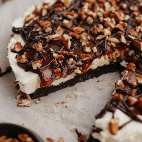 A no bake turtle cheesecake on parchment paper, one slice has been taken out.