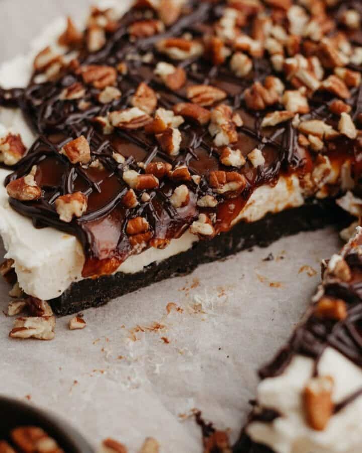 A no bake turtle cheesecake on parchment paper, one slice has been taken out.