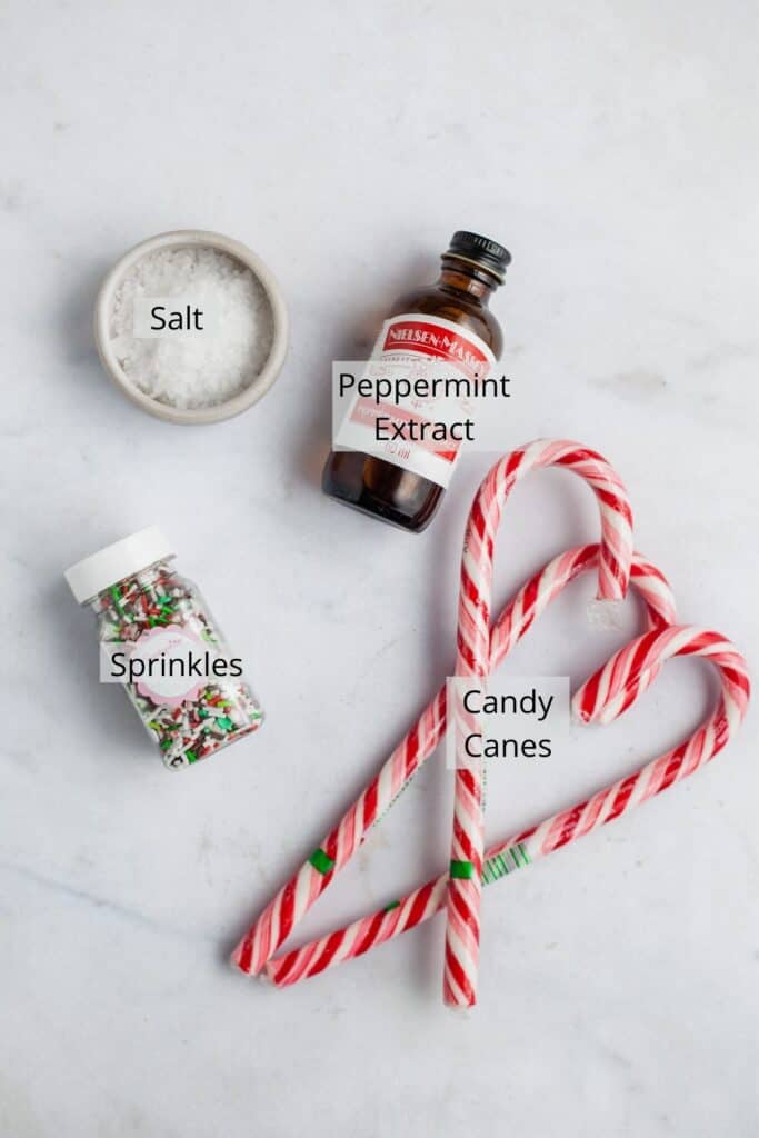 peppermint extract, three candy canes, sprinkles and a small bowl of salt on marble.