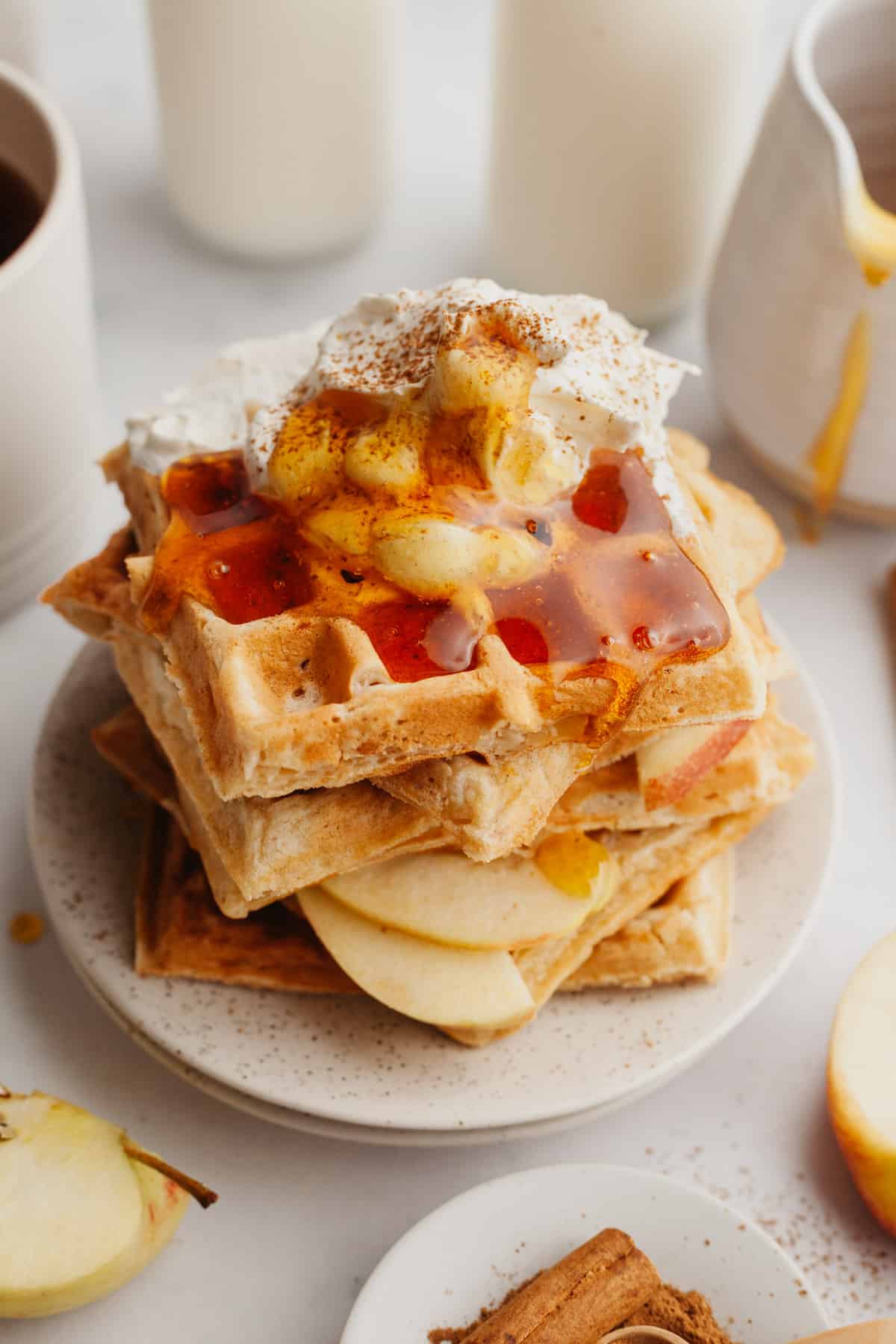 A stack of waffles with slices of apples and whipped cream.