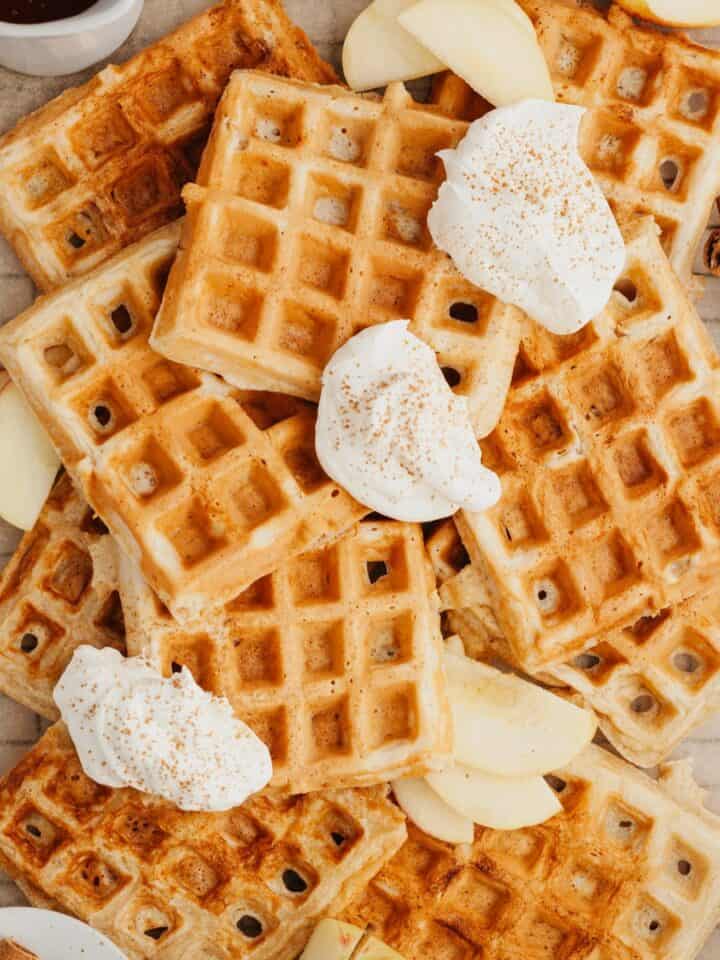 A stack of waffles with slices of apples and whipped cream.