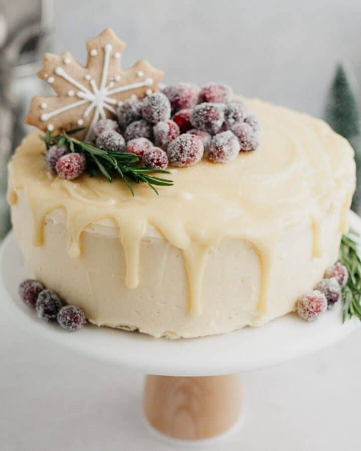 A white chocolate drip cake decorated with a gingerbread cookie and sugared cranberries.