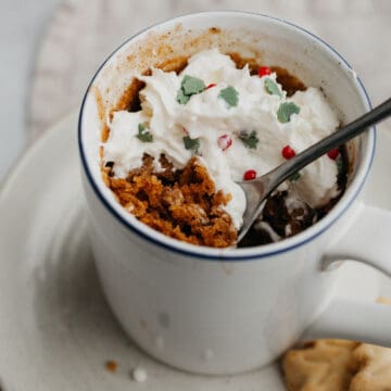 A gingerbread mug cake covered in whipped cream and Christmas sprinkles.