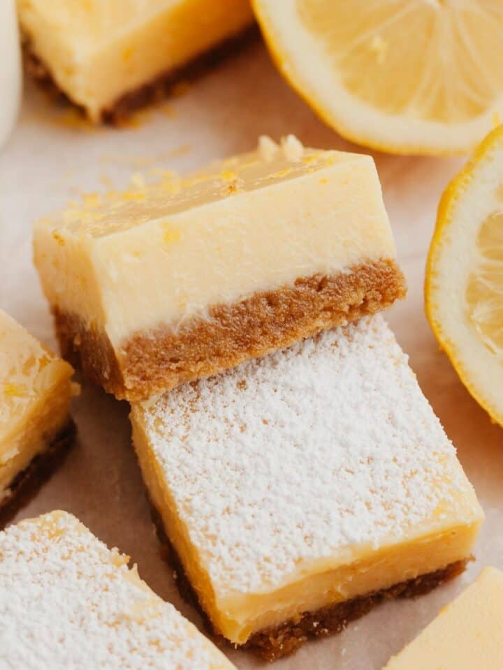 Lemon squares on parchment paper, some have been dusted with icing sugar.