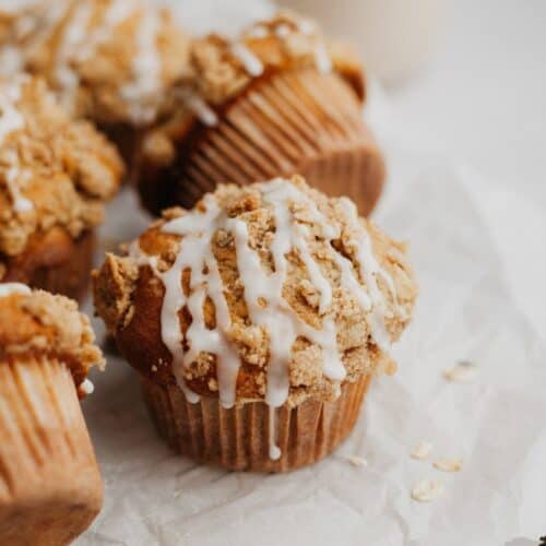several muffins drizzled with a glaze on top of parchment paper.