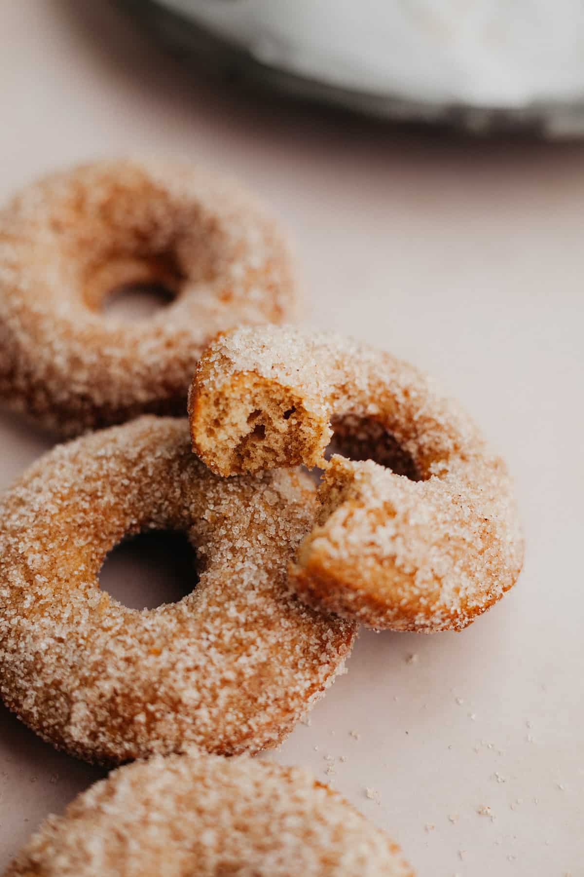 several cinnamon sugar doughnuts, one is resting on top with a bite taken out of it.