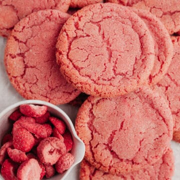 several pink sugar cookies on parchment paper with a small bowl of freeze dried strawberries.