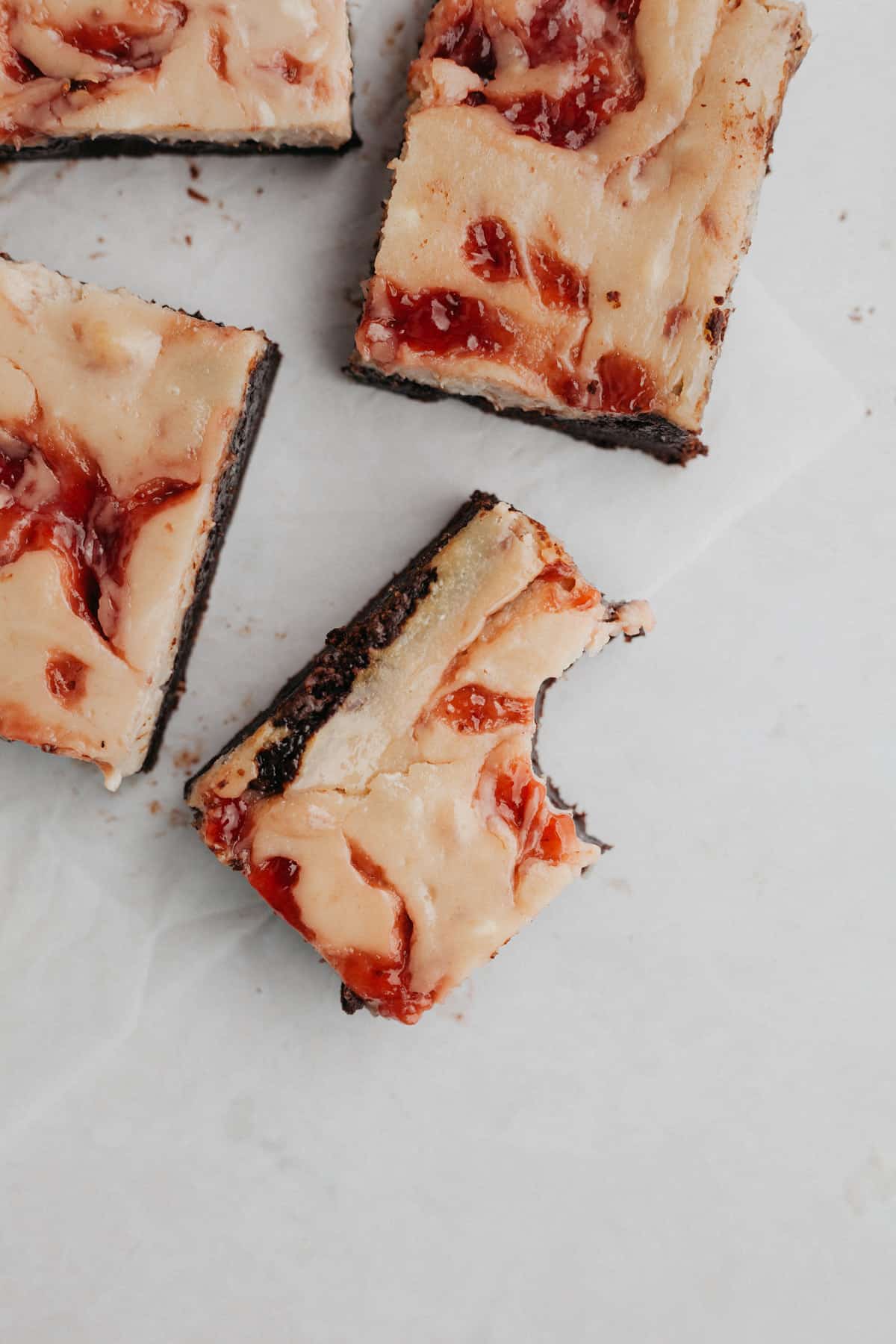 Several strawberry swirled cheesecake brownies on parchment paper.