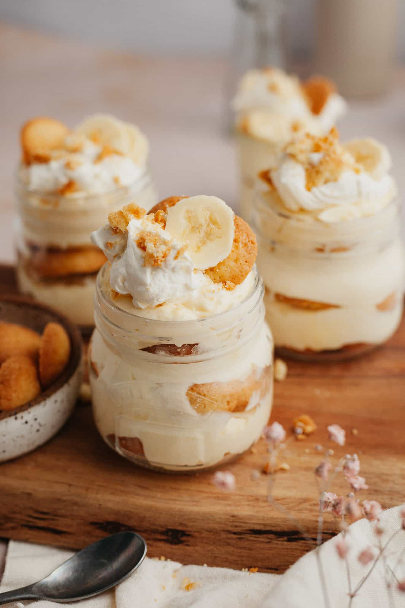 four jars of banana pudding on a wooden board.