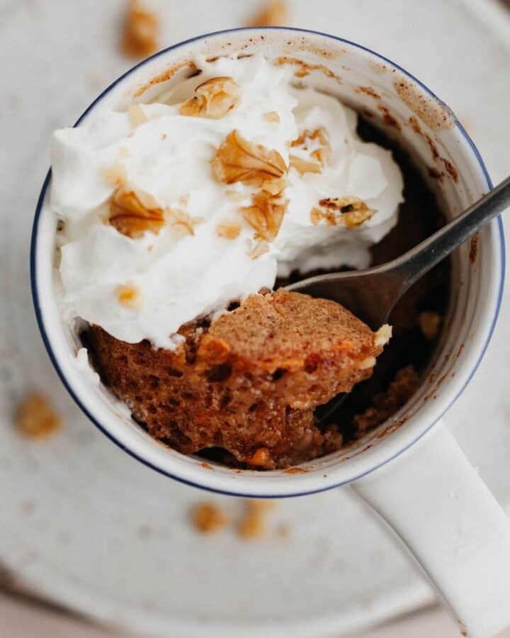 An overhead shot of a carrot mug cake topped with whipped cream.