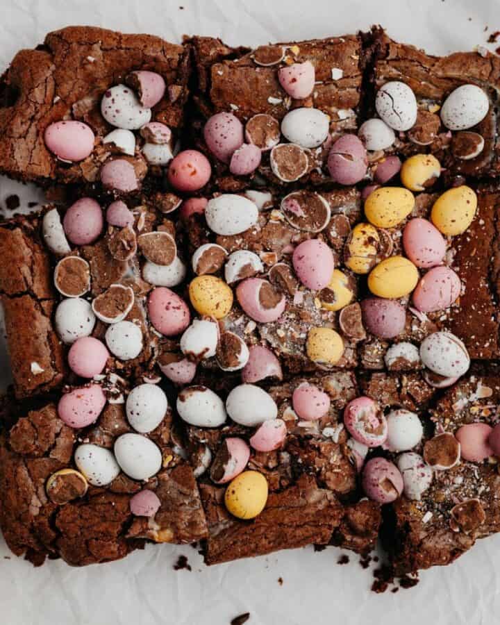 Sliced Easter brownies covered in mini eggs on parchment paper.