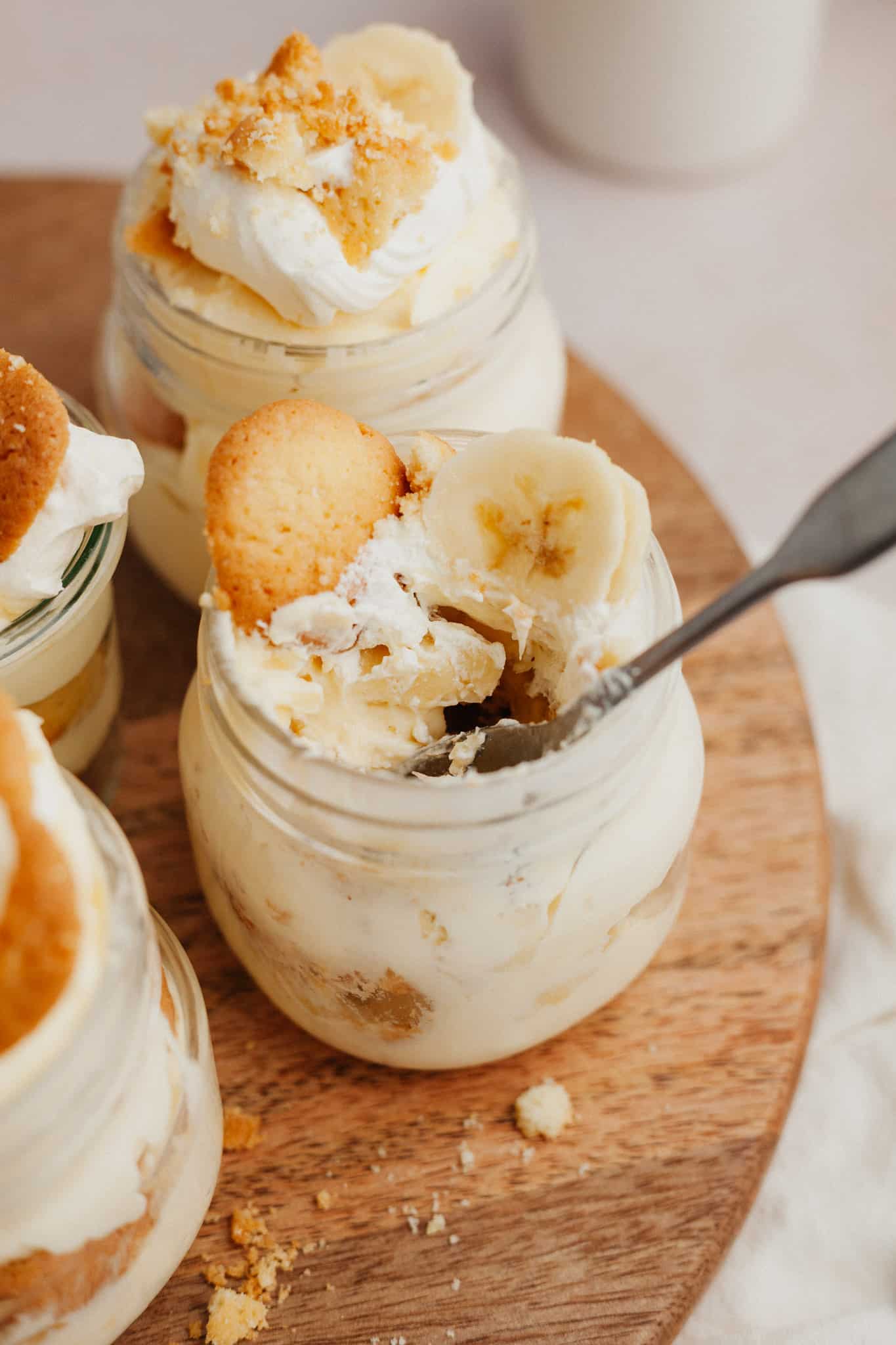 Banana pudding in a jar on a wooden board. There is a spoon in the jar
