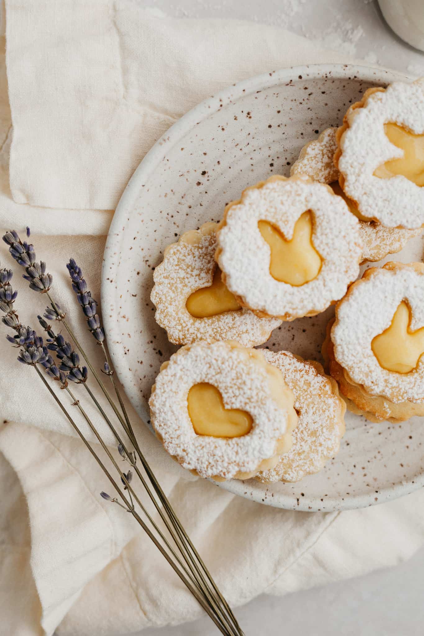 a small speckled beige plate with heart shaped lemon curd cookies dusted with confectioners' sugar.