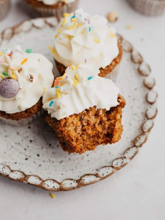 A small plate with three carrot cupcakes, one has a bite taken out of it.