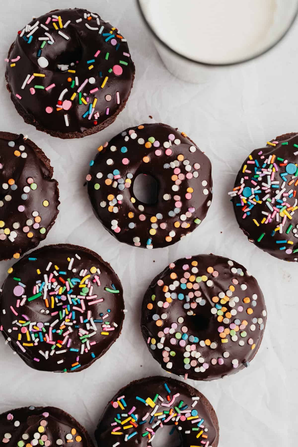 chocolate doughnuts with chocolate glaze and sprinkles on parchment paper.