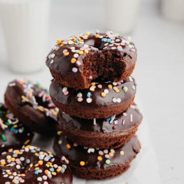 a stack of chocolate sprinkle donuts, the donut on top has a bite taken out of it.
