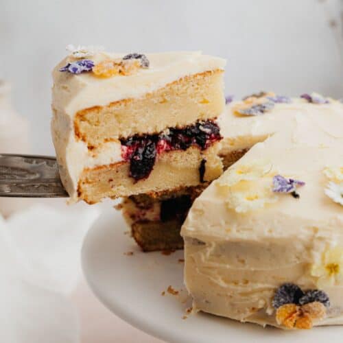 A yellow cake with a blueberry filling, a silver cake server is lifting one slice out.
