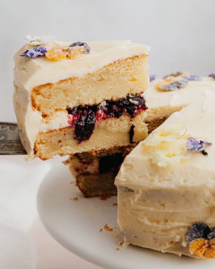 A yellow cake with a blueberry filling, a silver cake server is lifting one slice out.
