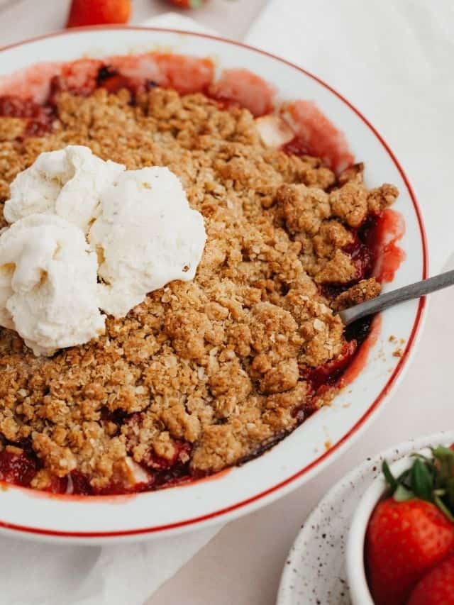 Strawberry and apple crisp in a white pie dish with several scoops of vanilla ice cream in the middle.