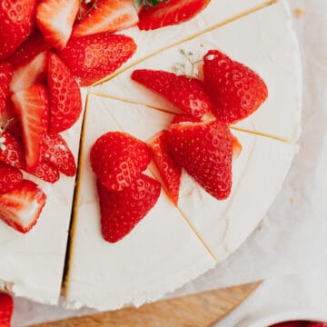 An overhead shot of a white cheesecake topped with sliced strawberries, three slices have been cut.