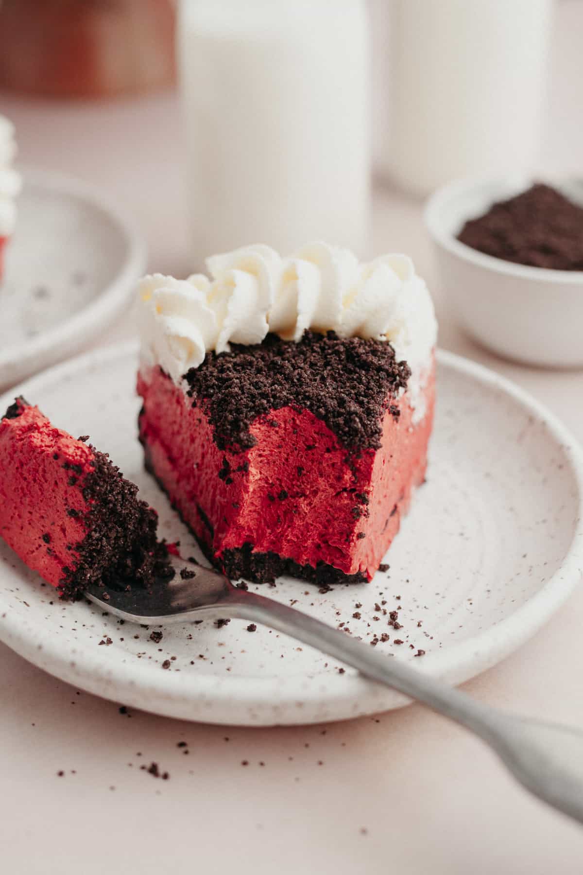 A slice of Oreo red velvet cheesecake on a small plate with a bite taken out of it.