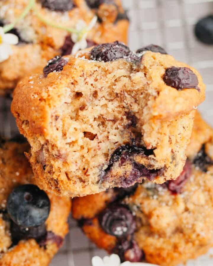 A close up of blueberry banana muffins, one has a bite taken out of it.
