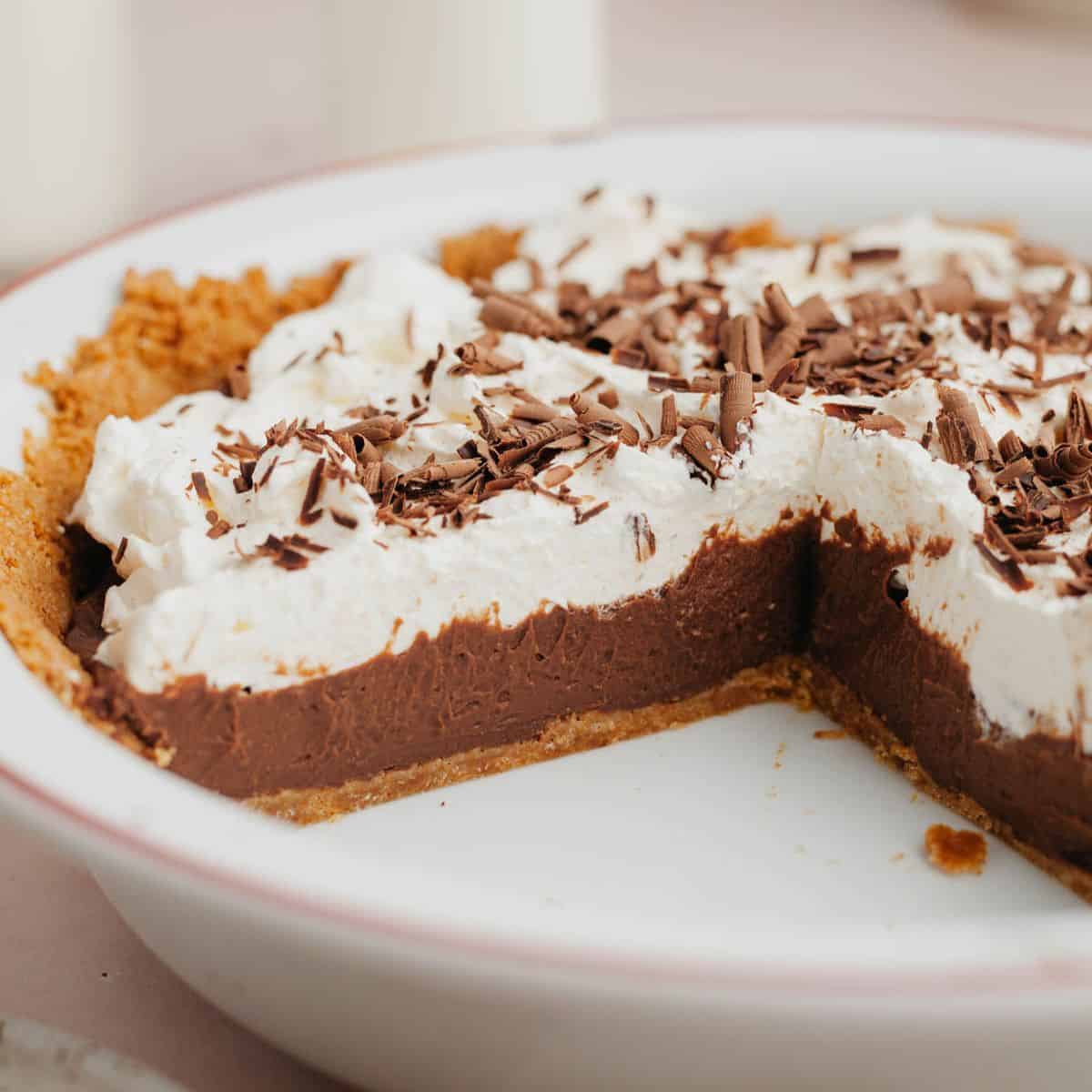 A chocolate pudding pie covered in whipped cream in a white pie dish.