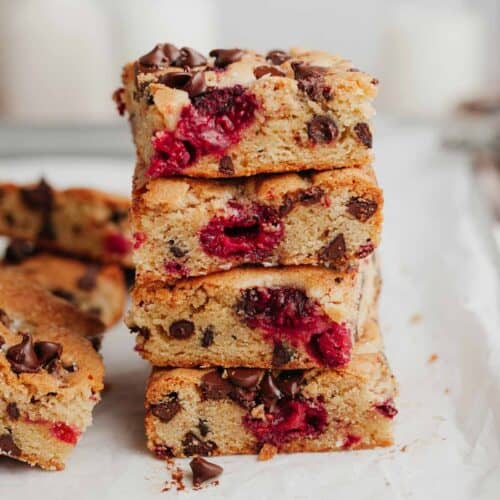 A stack of four raspberry blondies on parchment paper.