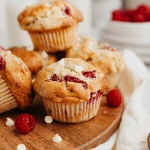 Several white chocolate raspberry muffins on a round wooden board.