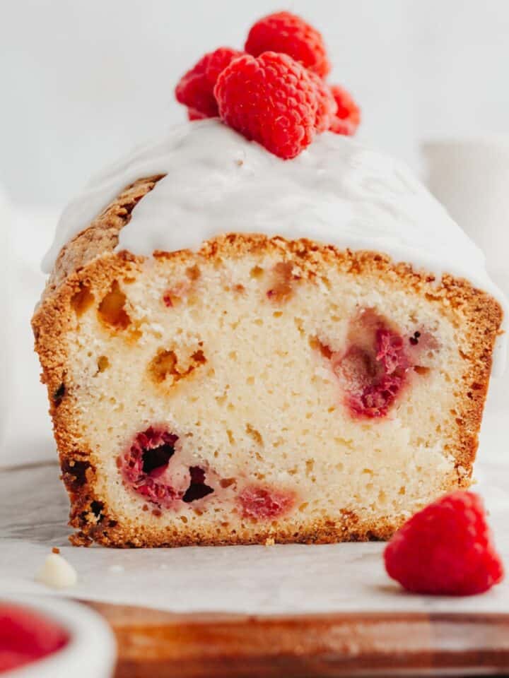 A raspberry loaf cake covered with a white glaze and fresh raspberries.