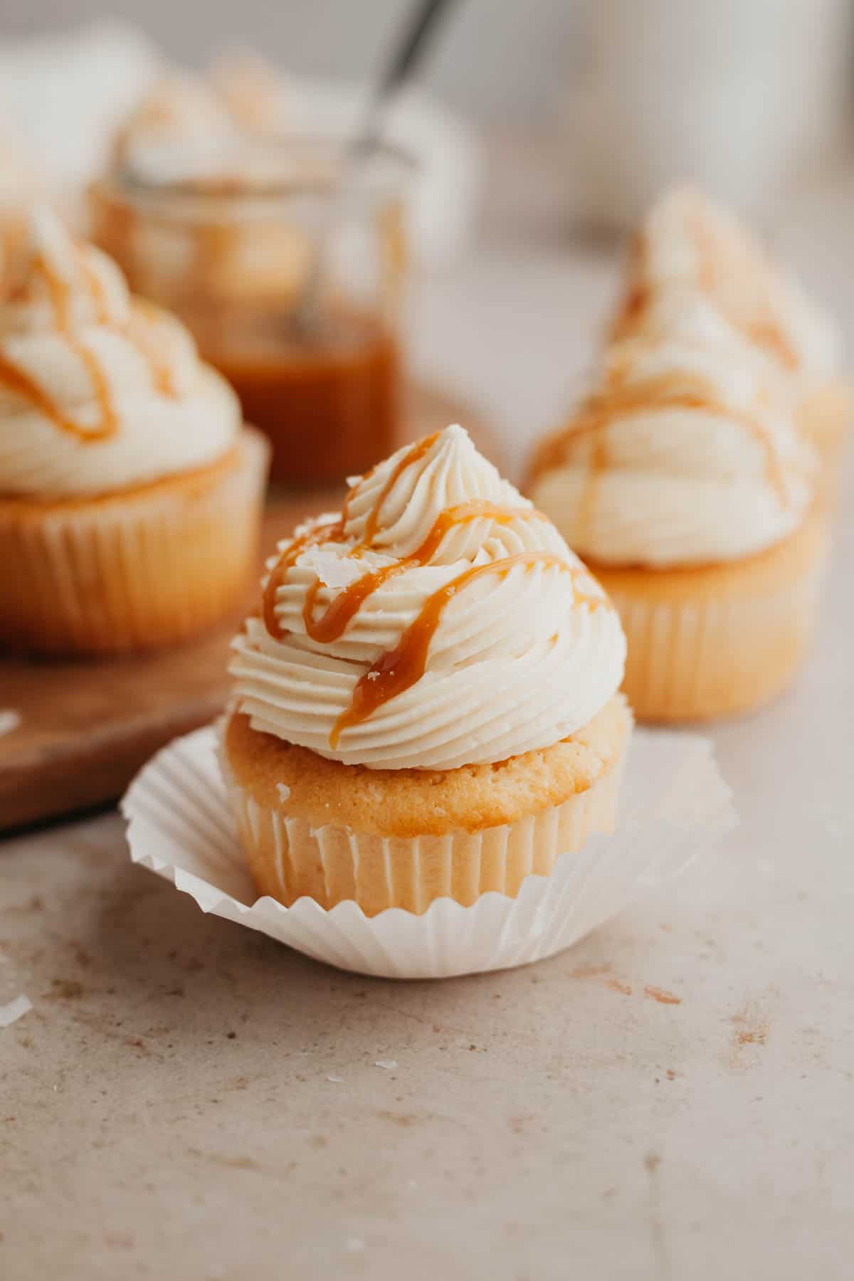 A caramel cupcake in a white paper liner, topped with buttercream and drizzled with caramel.
