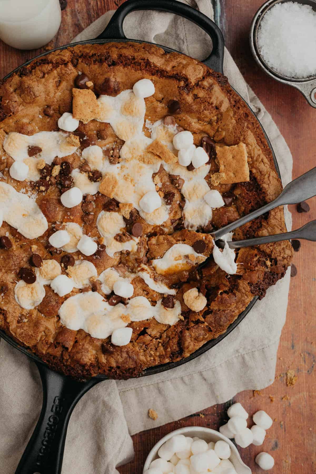A s'mores chocolate chip cookie skillet in a cast iron pan, there are two silver spins in the skillet.